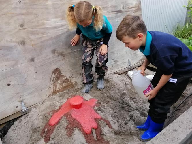 Children enjoying sandpit play making baking soda and vinegar volcano explosions