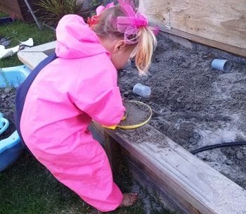 Girl in Mud Mates Coveralls making sandpit mud pies