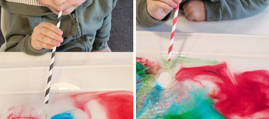 Puddle art idea for kids: Young child blowing through a straw onto coloured water